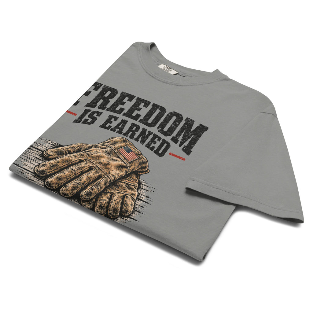 grey men's t-shirt with work gloves on a wooden surface, and above it says "Freedom is earned"